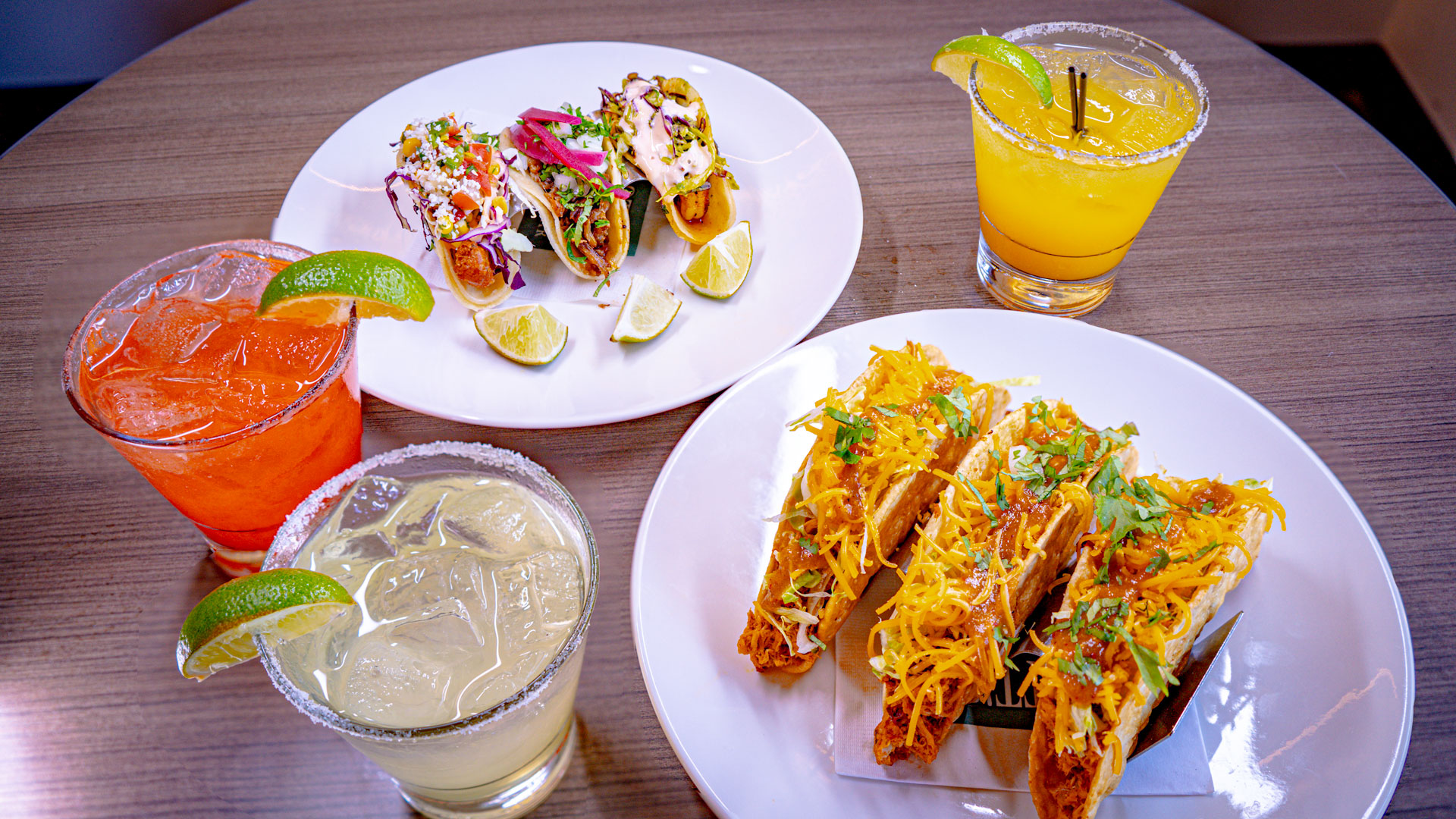 picture of two plates of tacos. A plate of soft corn tortilla street tacos loaded with Fish, Shrimp, and Carnitas. Another place filled with three crunchy tacos with chicken, cheddar cheese, pico and salsa.